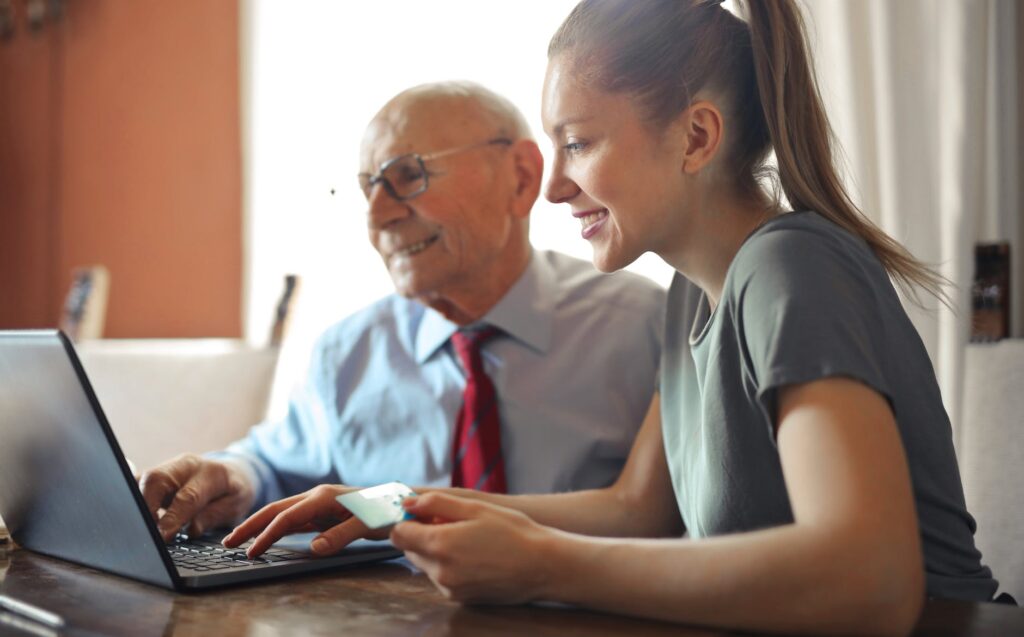 young woman helping senior man with payment on internet using laptop