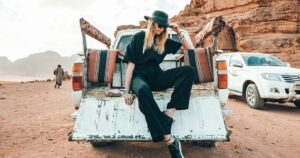 stylish woman sitting on car in desert area
